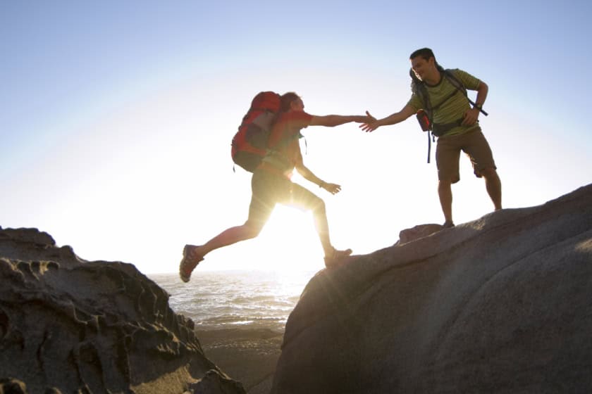 Hikers on cliff edges. One of them is jumping from one side to the other.