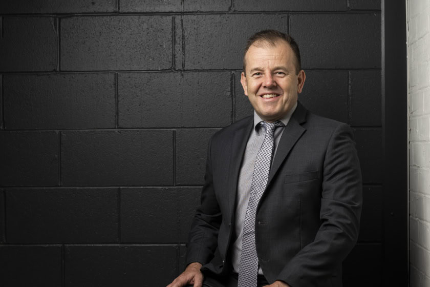 Matt Connor sitting down. Behind him is a black industrial wall.