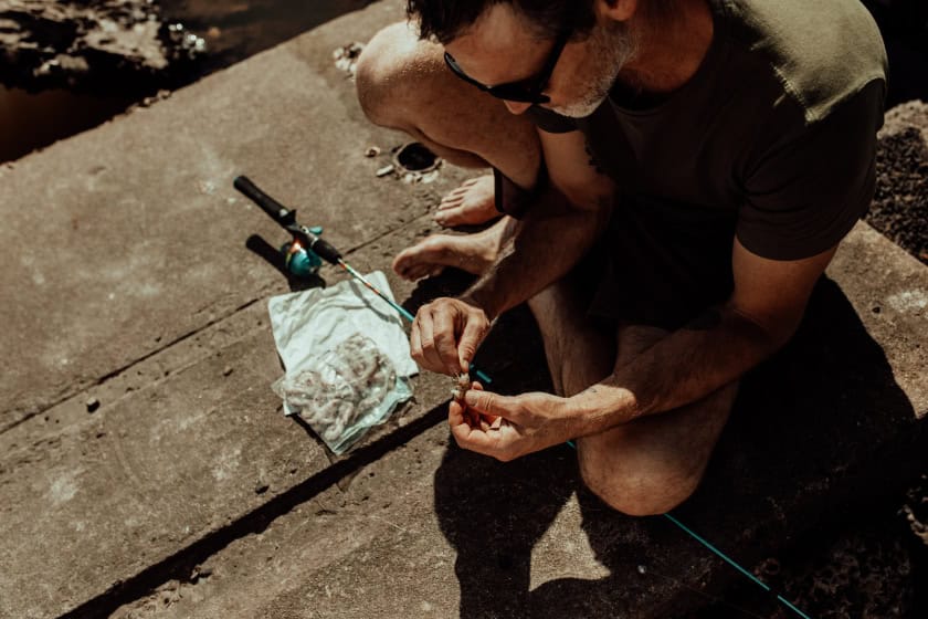 man sitting on the dock baiting his fishing hook