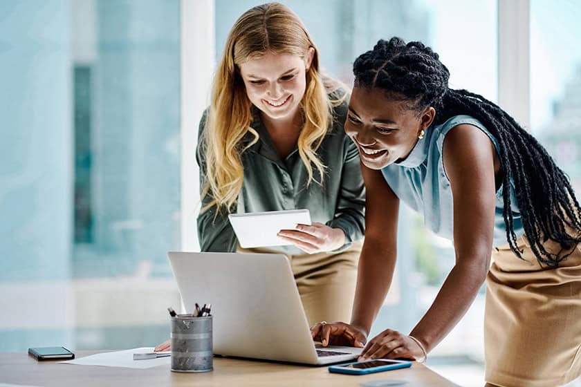 An accountant and a business owner look at a laptop screen. They are standing in an office and look happy.
